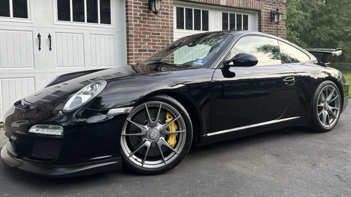 A black Porsche 911 GT3 on a driveway in front of a brick house